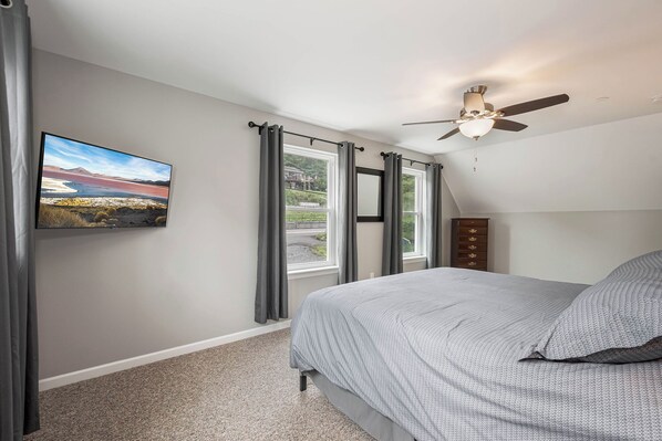 A bedroom with a bed, a ceiling fan, a window with curtains, and a painting on the wall.