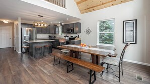 A spacious kitchen with a central island, dark cabinetry, and a dining area with a wooden table and benches. - Glencoe by Taylor Made Deep Creek (Oakland)