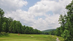 A golf course with a flagstick, surrounded by trees and hills in the background. - Golden Pond by Taylor Made Deep Creek (Swanton)