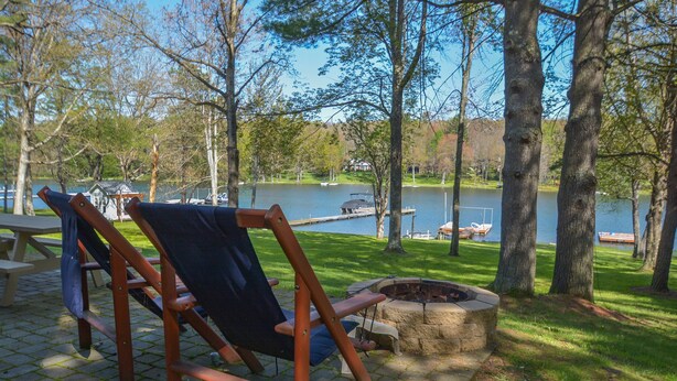 A wooden deck with a fire pit and a chair, overlooking a lake with boats and a dock. - Golden Pond by Taylor Made Deep Creek (Swanton)