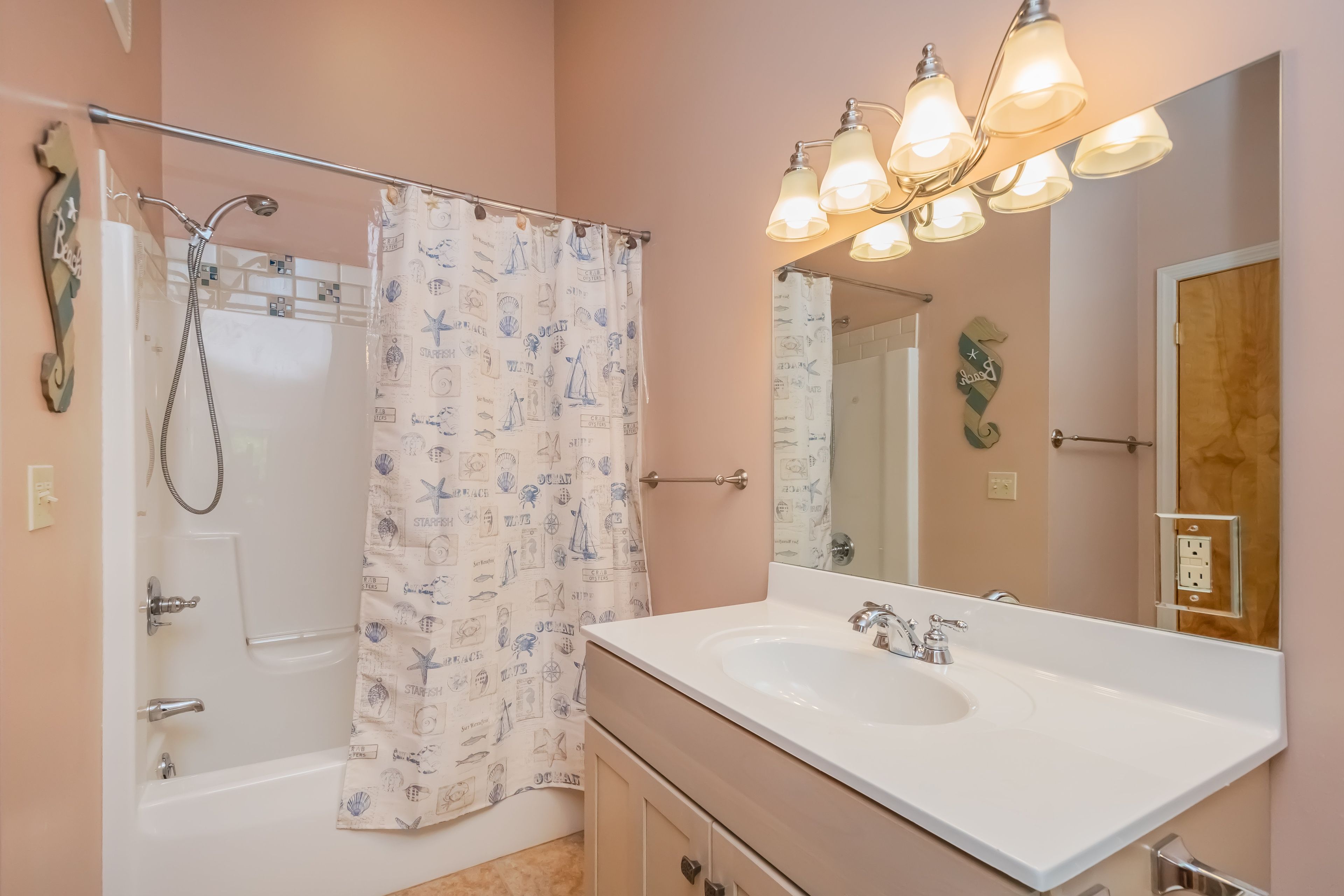 Une salle de bain équipée d’une douche, d’un lavabo, d’un miroir et d’un rideau de douche sur le thème de la marine.