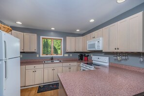 Una cocina moderna con armarios de colores claros, encimeras de granito, microondas integrado y ventana con vistas a zonas verdes.