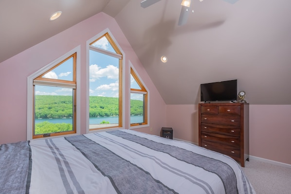 Ein Schlafzimmer mit einem großen Bett, einer Kommode, einem Fernseher und Seeblick durch Dachfenster.