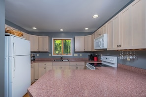 A kitchen with granite countertops, a refrigerator, a microwave, and a window with a view of trees. - Grande Villa by Taylor Made Deep Creek (Oakland)