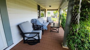 Une véranda abritée avec un espace salon comprenant un canapé et des fauteuils, ainsi qu’une plante en pot.