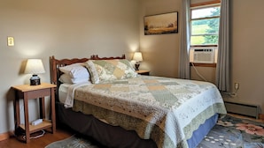 Une chambre à coucher avec un lit, deux tables de chevet, une commode, une fenêtre avec des rideaux et un tableau au mur.