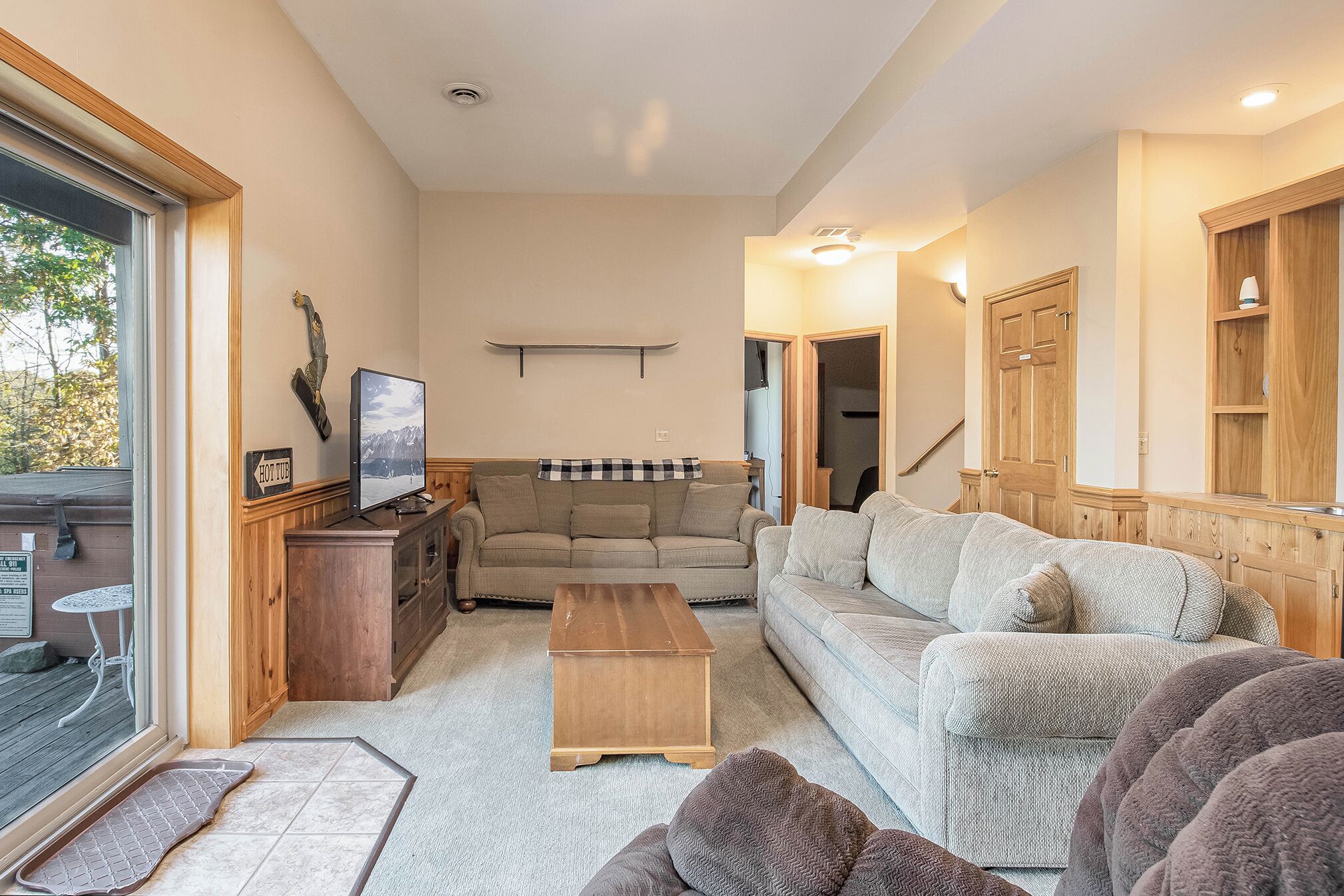 A cozy living room with a sofa, coffee table, and TV. There is a wooden cabinet and a window with a view of the outdoors.