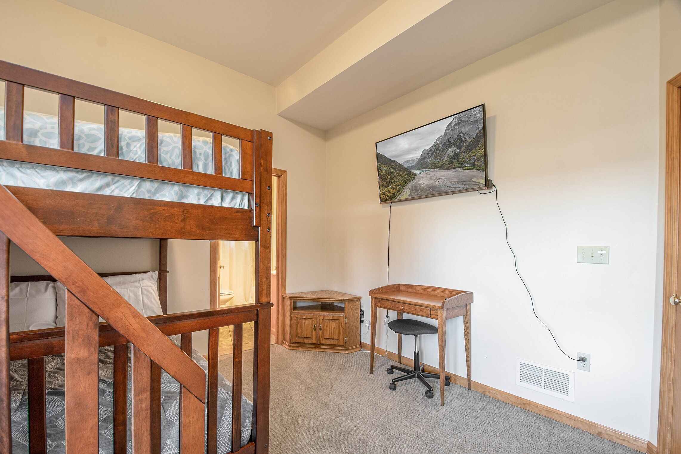 A bedroom with a bunk bed, a desk, and a mounted TV.