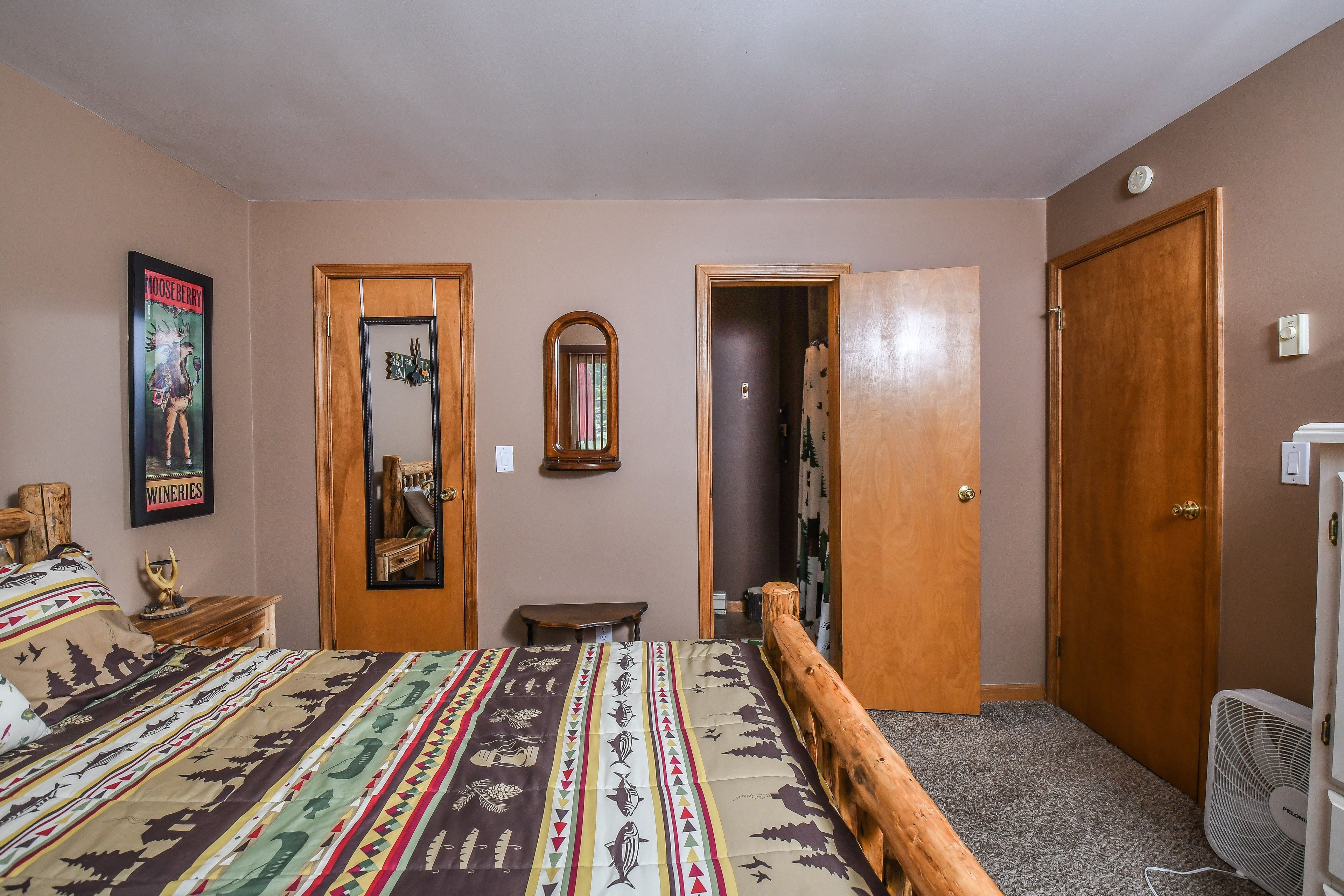 Un dormitorio con cama, cabecera de madera, espejo, puerta y ventilador.