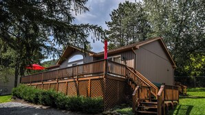 Une cabane en bois avec une terrasse, un escalier et un parasol rouge.
