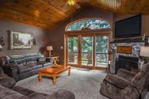 A cozy living room with a fireplace, leather furniture, and a large window overlooking a deck. - Happy Landing by Taylor Made Deep Creek (McHenry)