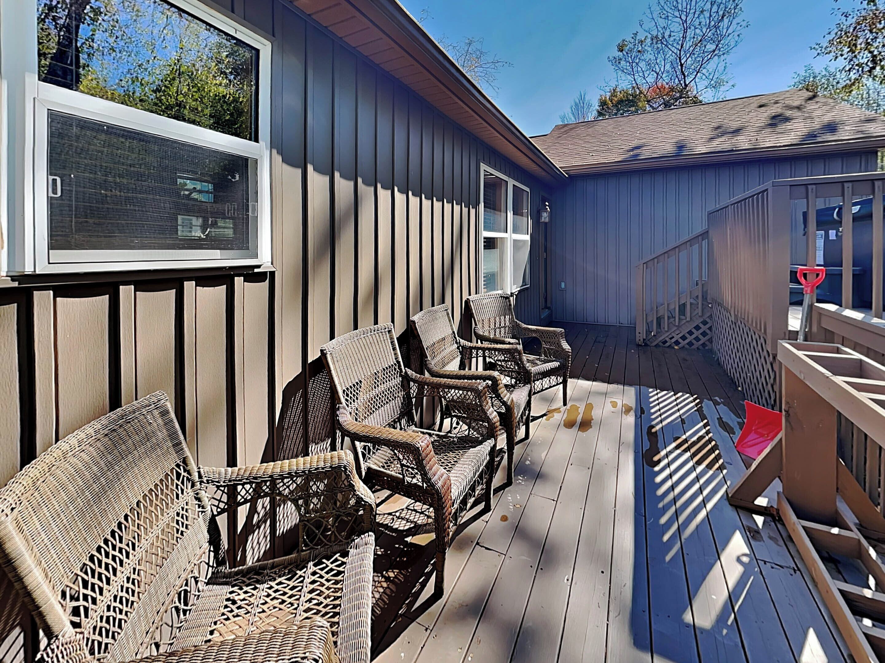 A covered outdoor deck with wicker furniture and a wooden railing.