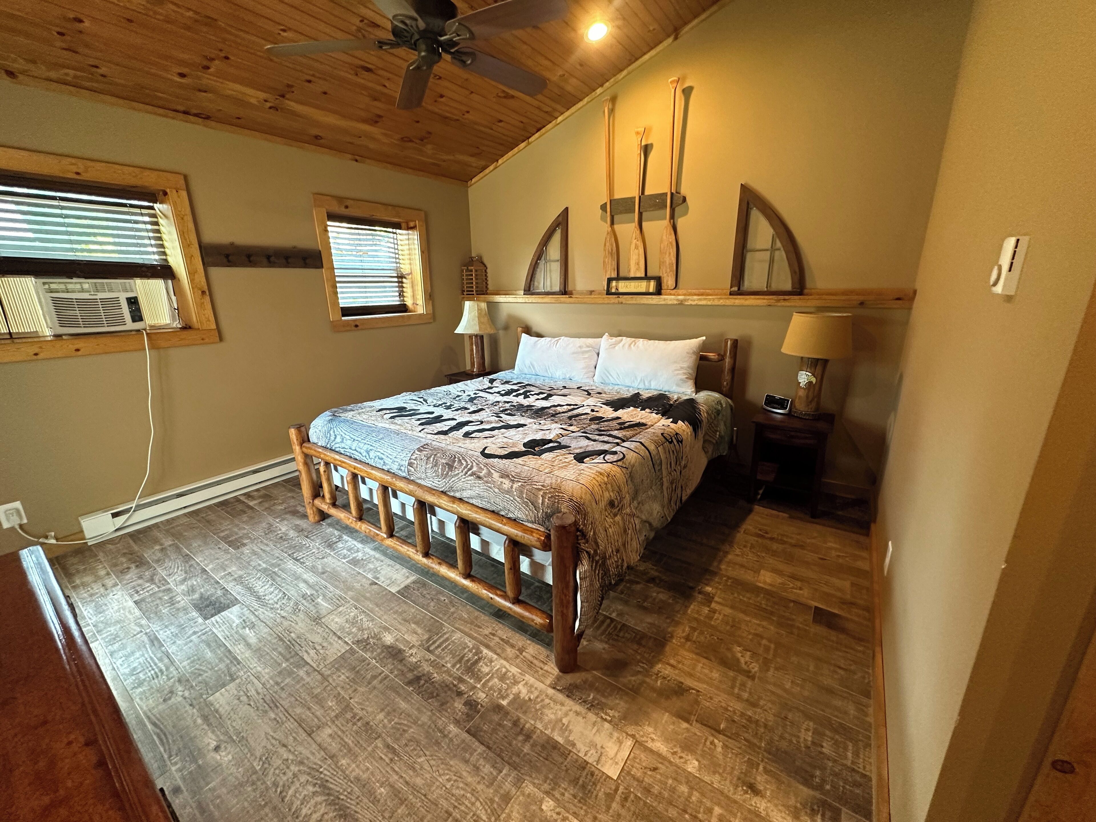A bedroom with a wooden bed frame, a ceiling fan, two bedside lamps, and a window with blinds.