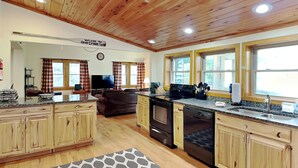 A spacious kitchen with wooden cabinets, a central island, and a dining area with a couch. - Happy Trails by Taylor Made Deep Creek (Oakland)