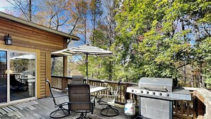 A wooden deck with outdoor furniture, a grill, and a glass door leading to an interior space. - Happy Trails by Taylor Made Deep Creek (Oakland)