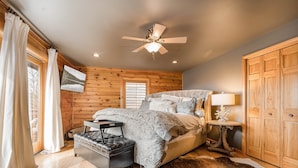 A bedroom with a bed, a ceiling fan, a wooden wardrobe, and a window with curtains.