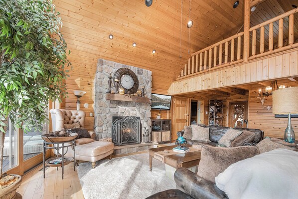 A cozy cabin interior with a stone fireplace, wooden ceiling, and a balcony. - Happyplace Hideaway by Taylor Made Deep Creek (McHenry)