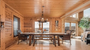 A wooden cabin interior with a large dining table, benches, and a chandelier.