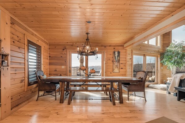 A wooden cabin interior with a large dining table, benches, and a chandelier. - Happyplace Hideaway by Taylor Made Deep Creek (McHenry)