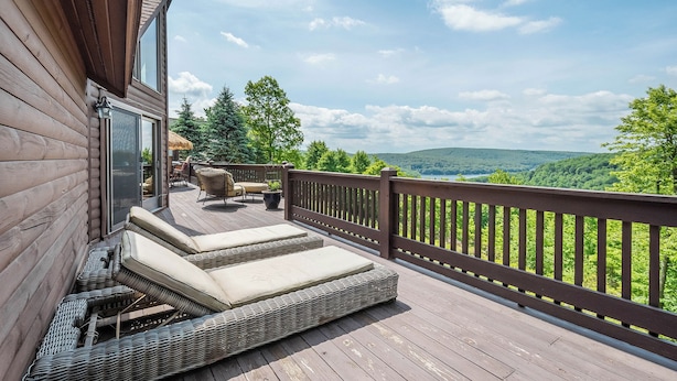 A wooden deck with outdoor seating, a glass door, and a view of a forested landscape.