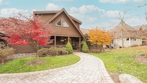 A log cabin with a curved driveway, surrounded by autumn foliage and a well-maintained lawn.