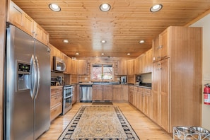 A modern kitchen with wooden cabinets, stainless steel appliances, and a patterned rug. - Happyplace Hideaway by Taylor Made Deep Creek (McHenry)