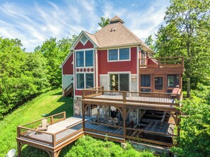 A two-story house with a deck, large windows, and a stone foundation. - Hawk Mountain by Taylor Made Deep Creek (McHenry)