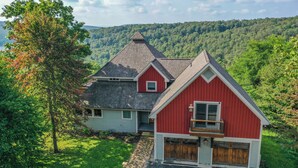 A two-story house with a red and white exterior, a sloped roof, and a view of a forested hillside. - Hawk Mountain by Taylor Made Deep Creek (McHenry)