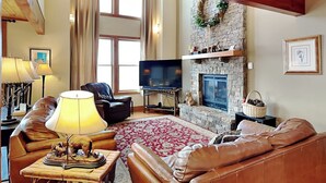 A cozy living room with a stone fireplace, leather sofas, a television, and a large window. - Hawk Mountain by Taylor Made Deep Creek (McHenry)