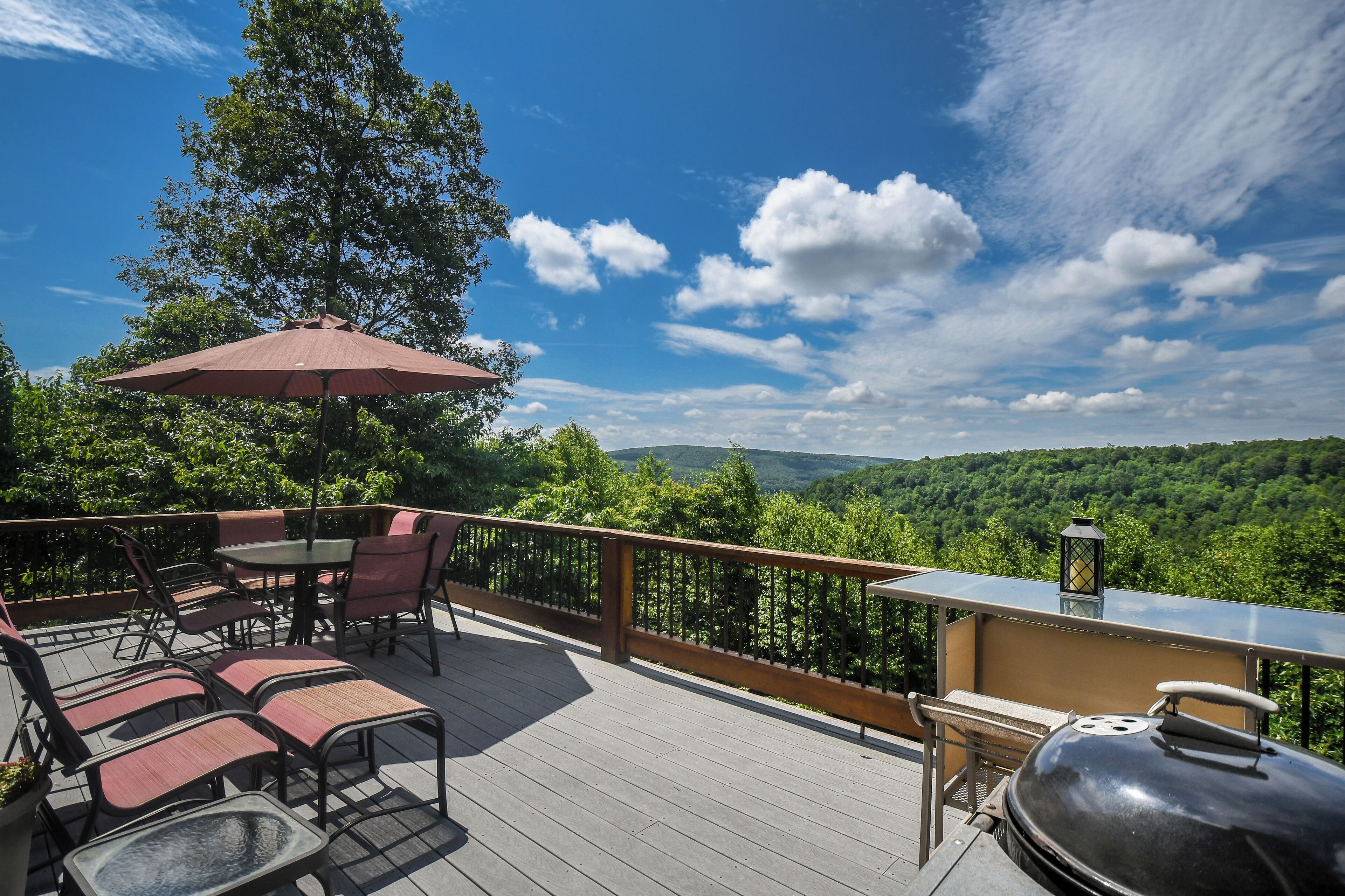 Eine Terrasse mit Gartenmöbeln, einem Grill und Blick auf eine bewaldete Landschaft.