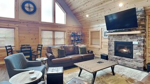Ett mysigt vardagsrum med en lädersoffa, ett soffbord och en platt-TV som är monterad på väggen ovanför en eldstad i sten.