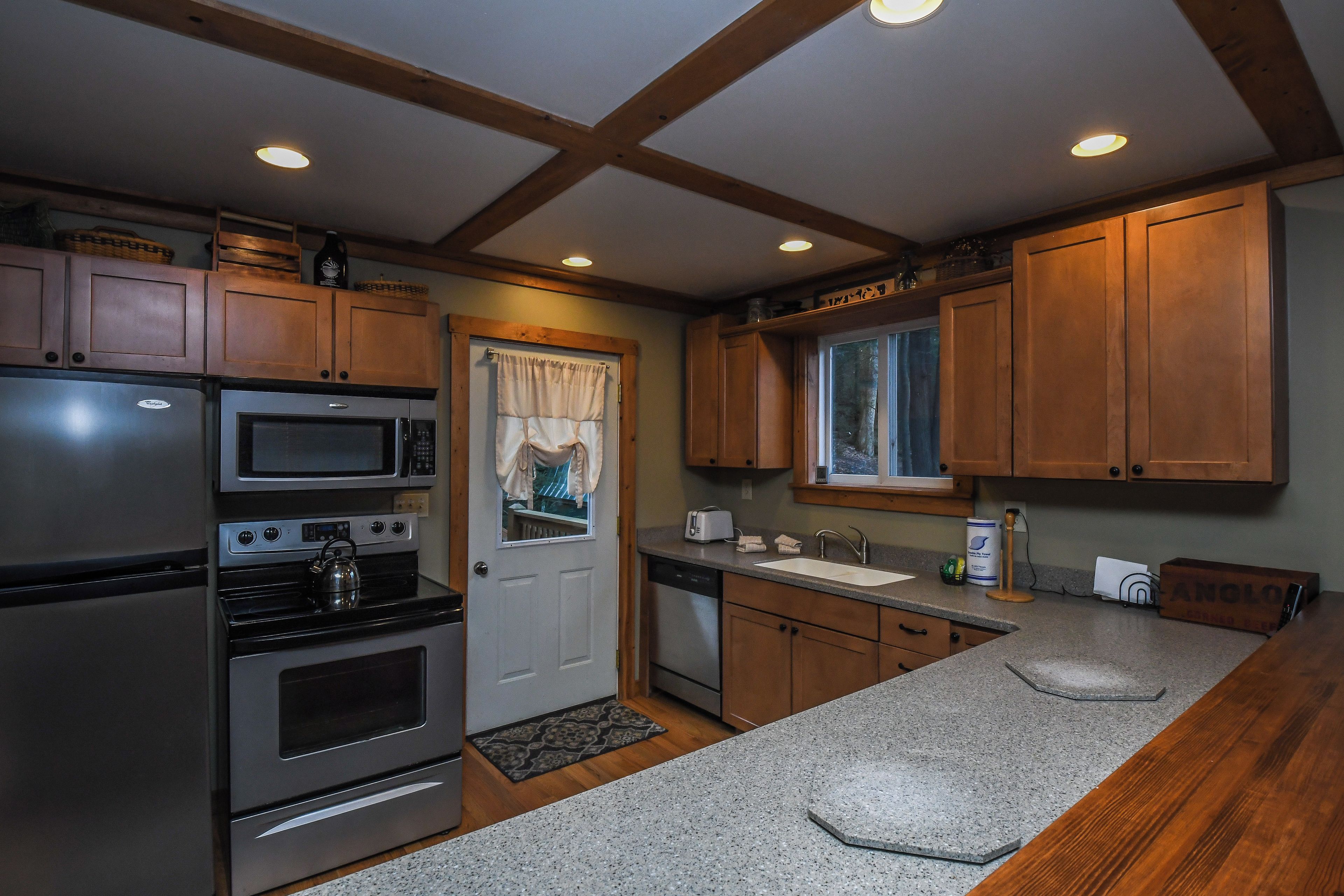 A kitchen with wooden cabinets, stainless steel appliances, a window with curtains, and a granite countertop.
