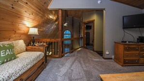 Ein gemütliches Zimmer mit Holzbalkendecke, einer Couch mit floralem Bettbezug, einer Lampe, einer Holzkombination und einem Fernseher.
