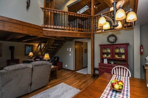 Un vaste espace de vie agrémenté d’un escalier en bois, d’une table à manger avec un panier de fruits et d’un buffet rouge aux portes vitrées.