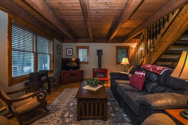 Ein gemütliches Wohnzimmer mit Holzbalkendecke, einem Ledersofa, einem Couchtisch und einem Fernseher.
