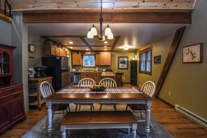 A dining area with a wooden table, chairs, and a bench. There is a kitchen in the background with wooden cabinets and a refrigerator. - Hideaway by Taylor Made Deep Creek (Oakland)