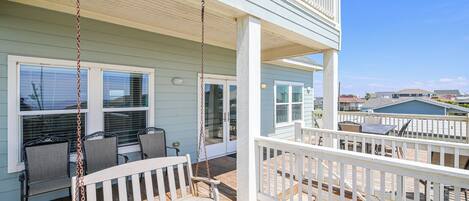 A covered outdoor area with a wooden deck, a white swing, and a white railing.