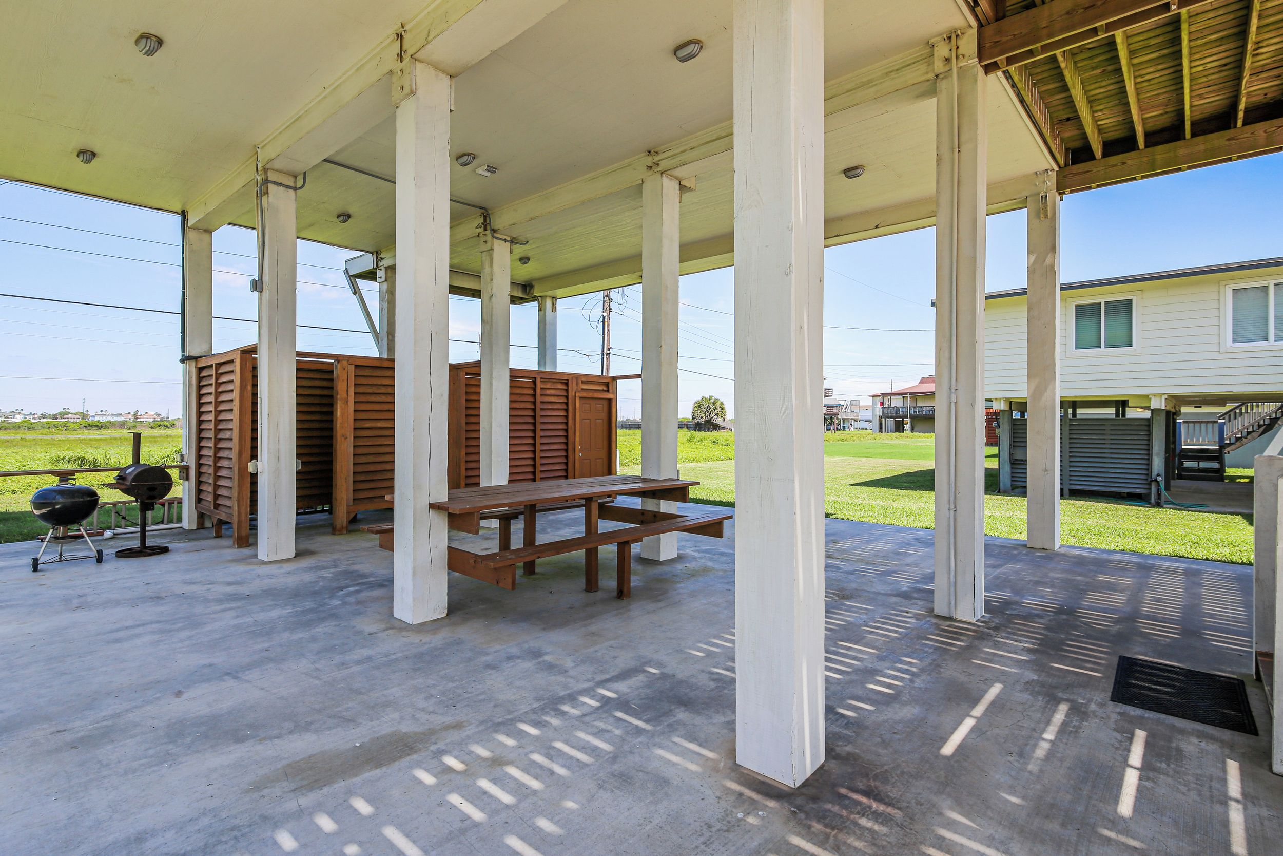 An outdoor covered patio with a concrete floor, wooden benches, and a barbecue grill.