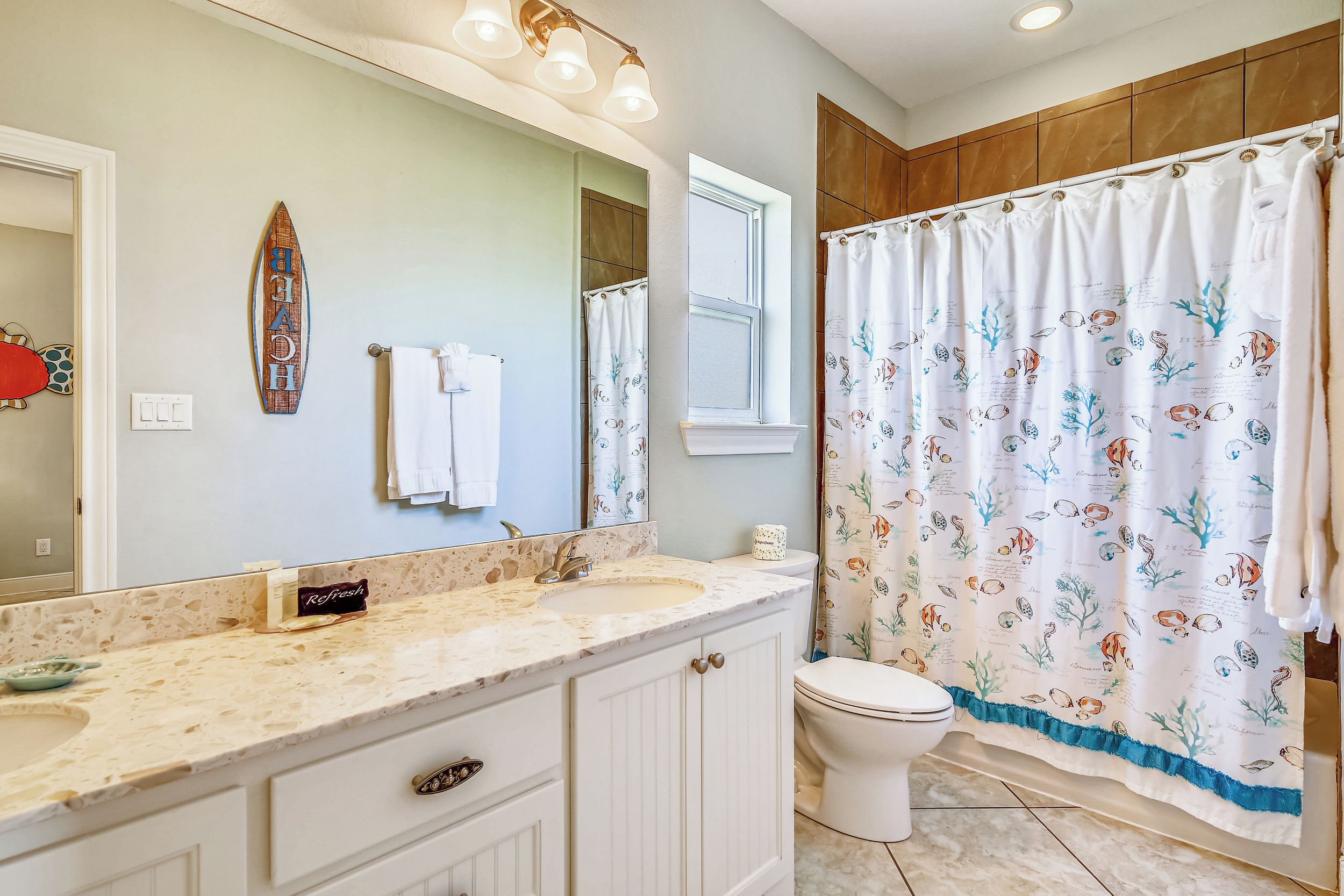 A bathroom with a marble countertop, a large mirror, a toilet, and a shower curtain with a marine theme.