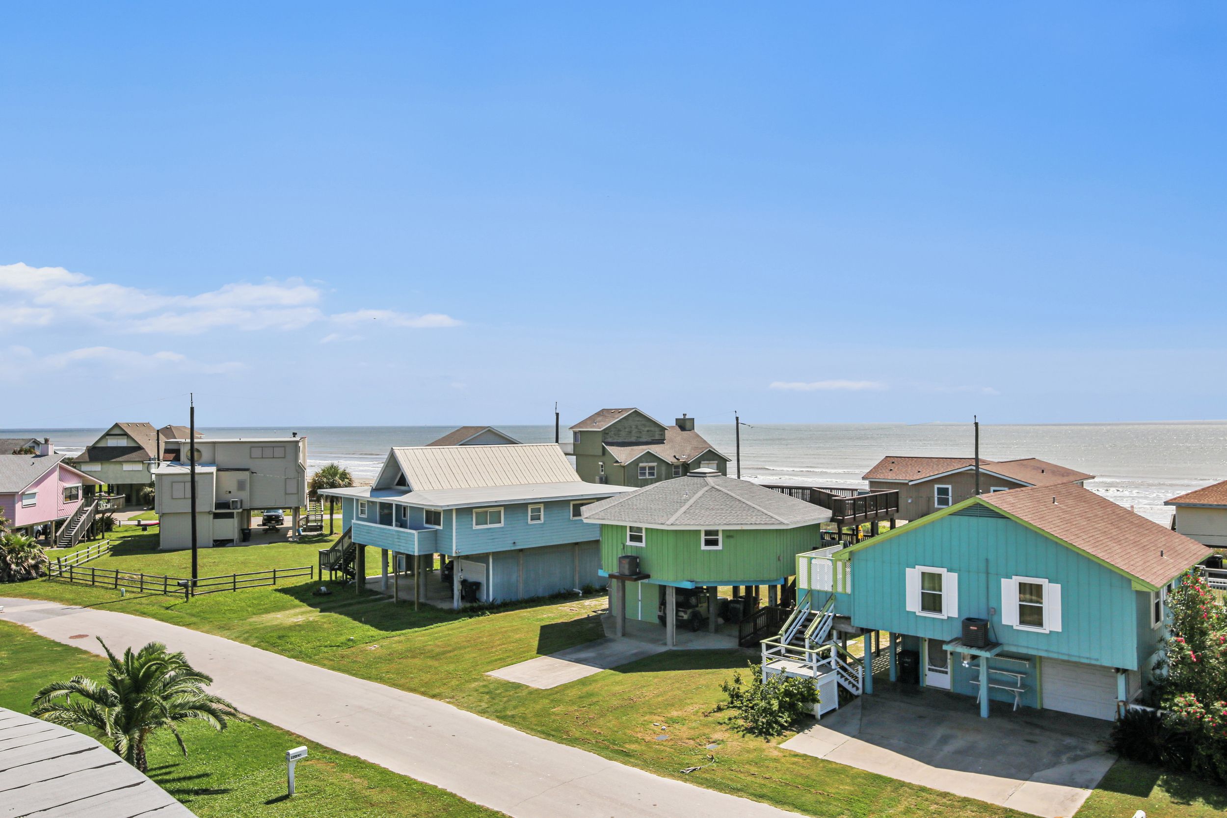 A coastal residential area with houses, a sidewalk, and a view of the ocean.