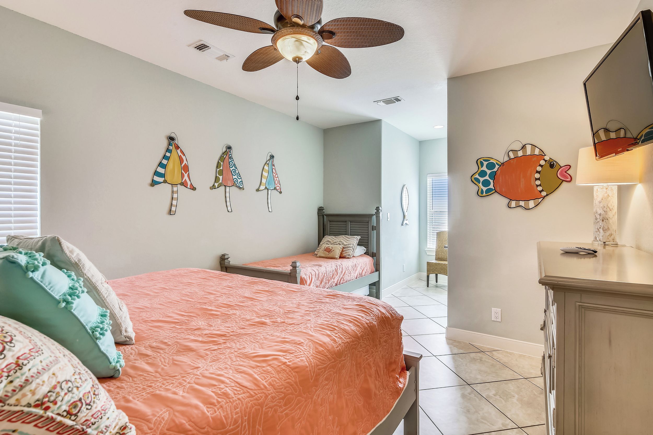 A bedroom with two beds, a ceiling fan, and decorative wall art.