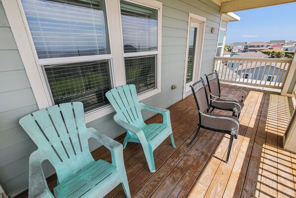 A wooden deck with two turquoise Adirondack chairs and two metal chairs.