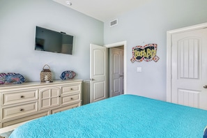 A bedroom with a bed, dresser, TV, and a door. - A Salty Kiss by Ryson Vacation Rentals (Galveston)