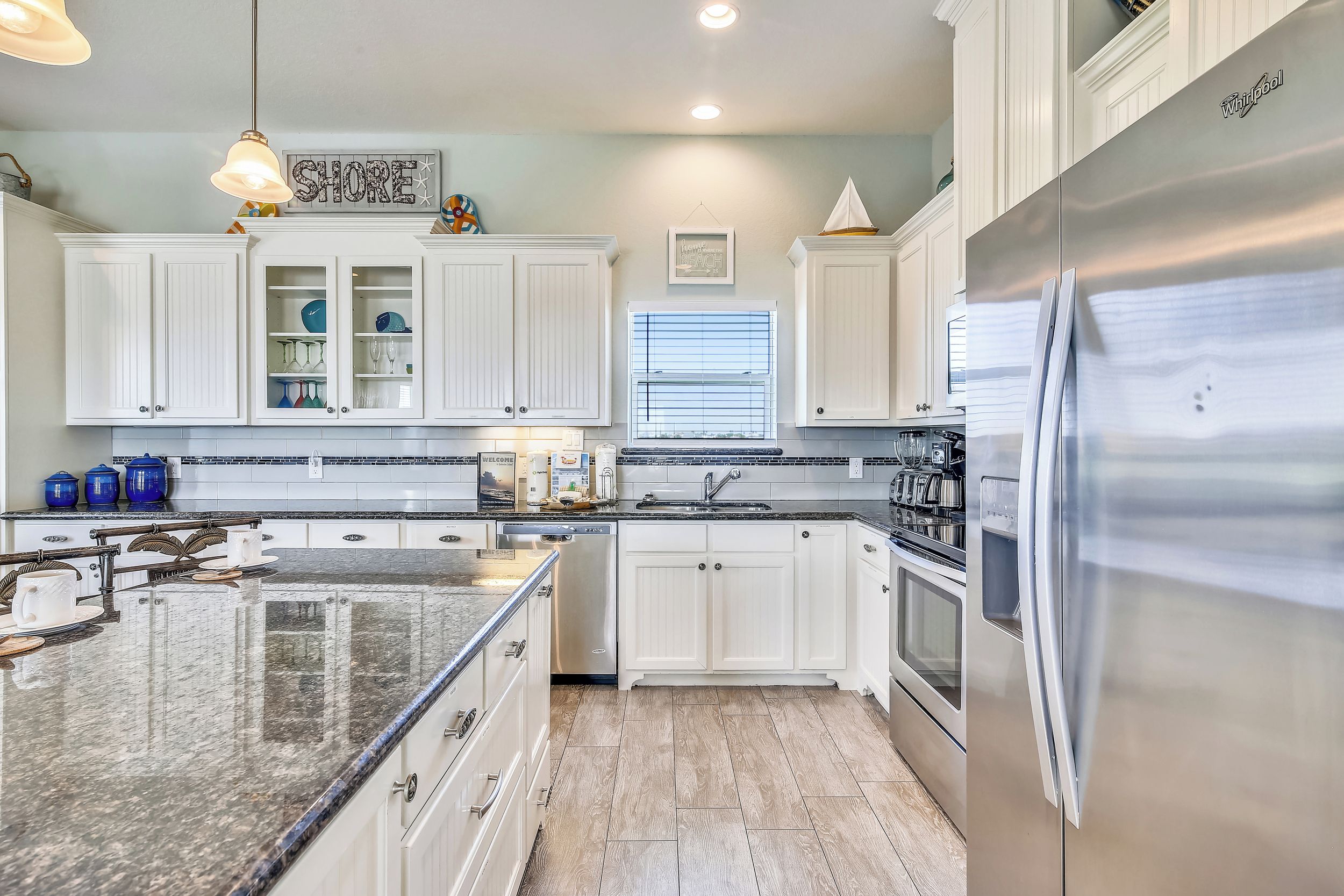 A modern kitchen with white cabinetry, a stainless steel refrigerator, and a granite countertop.