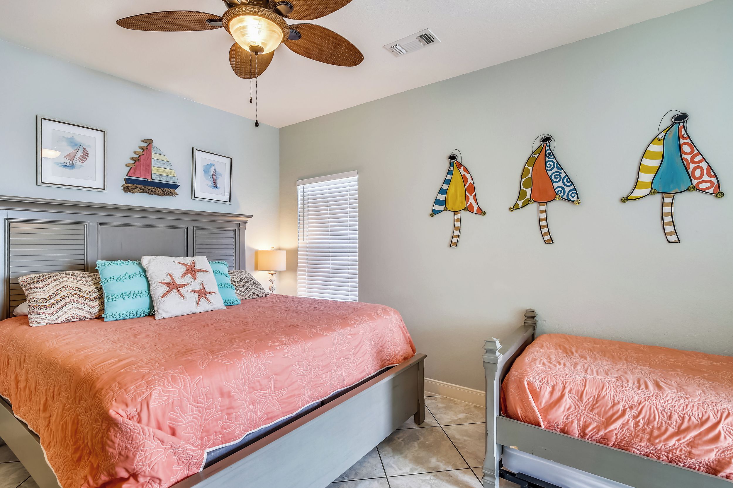Un dormitorio con cama, mesita de noche, ventilador de techo y decoraciones en la pared, incluyendo cuadros enmarcados y adornos colgantes de colores.