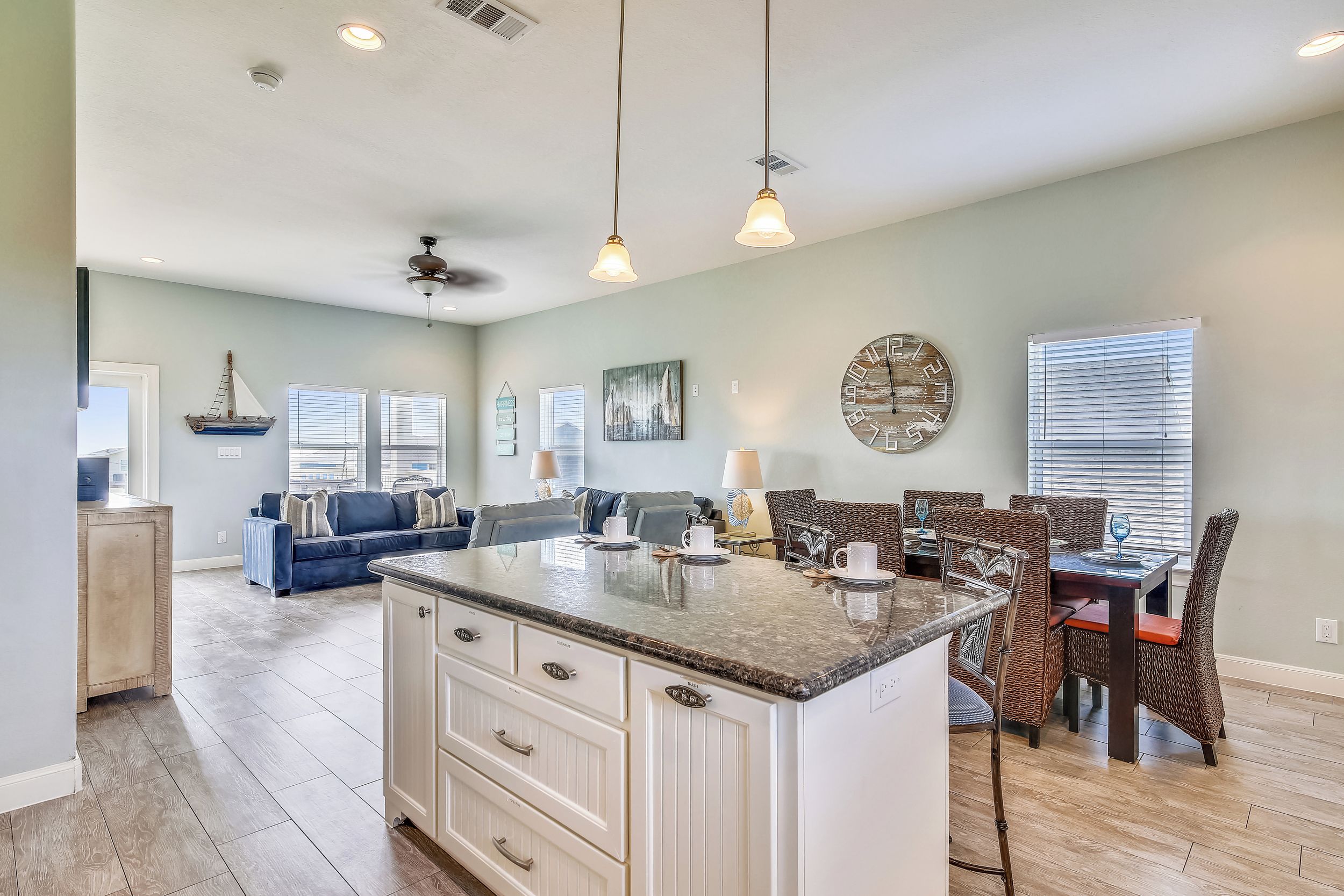 A spacious kitchen with a central island, dining area with wicker chairs, and a living room with a blue sofa.