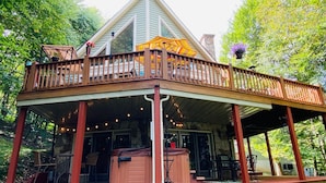 A covered outdoor deck with a wooden railing, a hot tub, and string lights. - Heart and Soul by Taylor Made Deep Creek (Oakland)