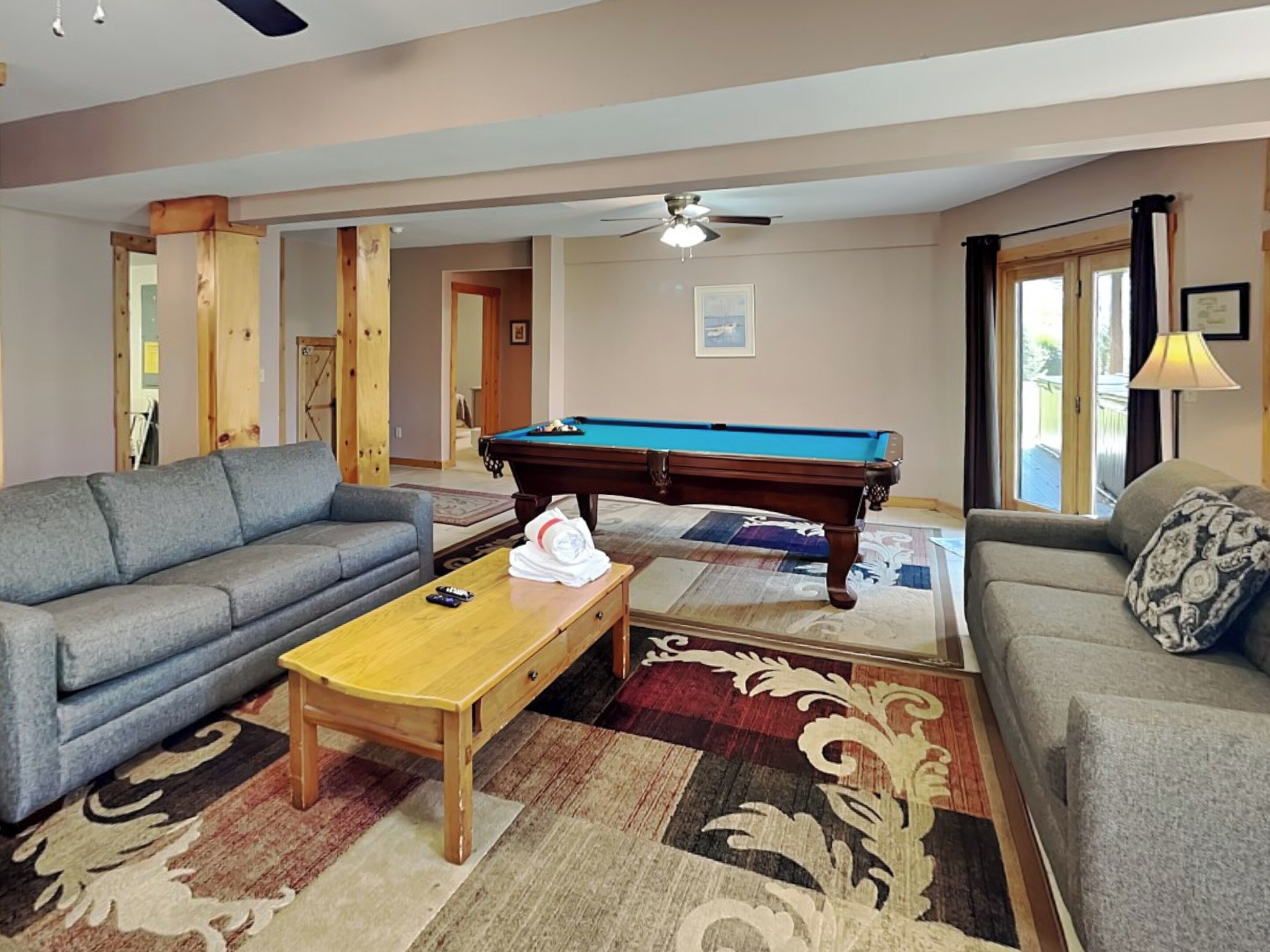 A living room with a pool table, two sofas, a coffee table, and a ceiling fan.