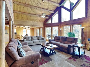 A spacious living room with wooden walls and ceiling, large windows, and a ceiling fan. - Heart's Desire by Taylor Made Deep Creek (McHenry)