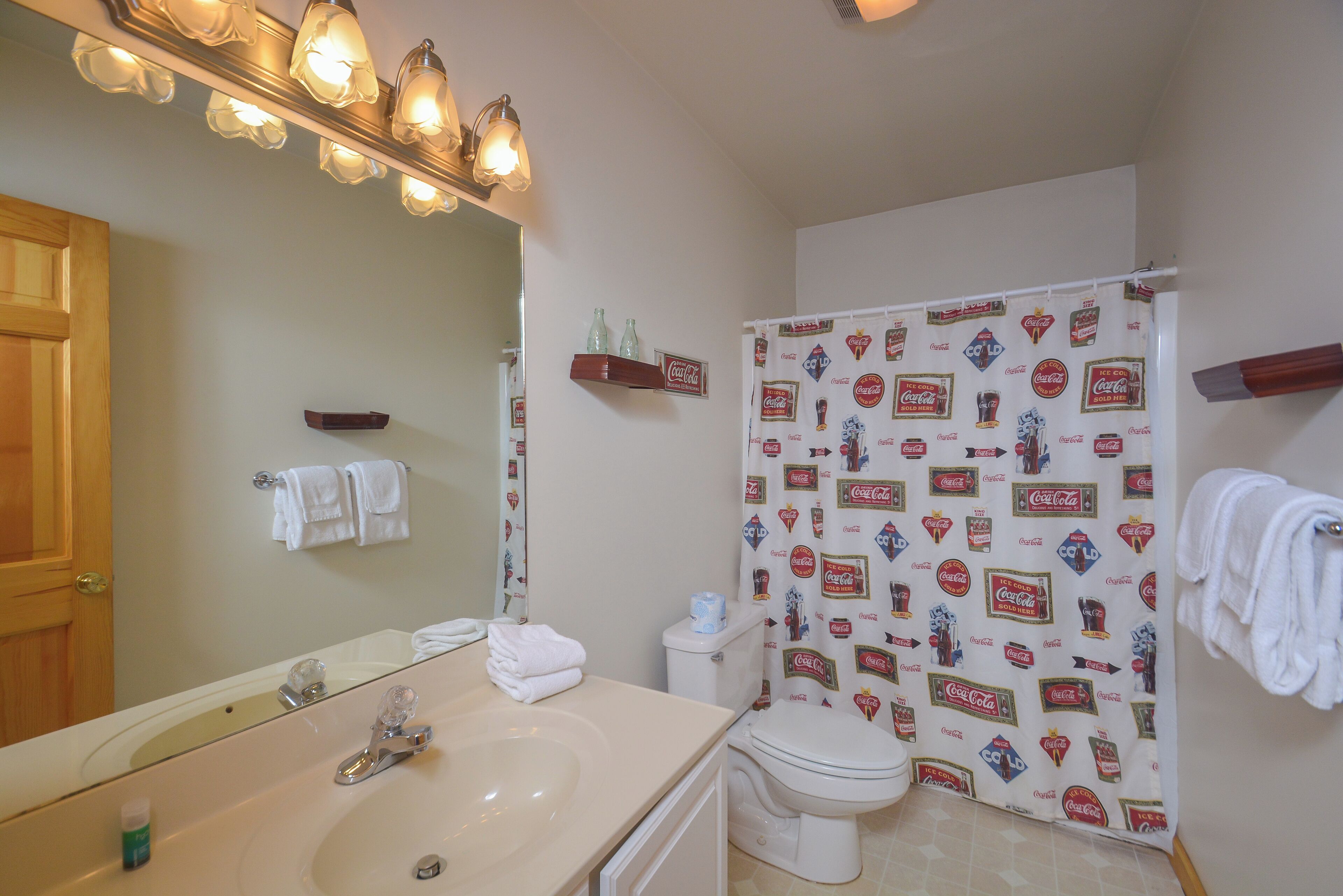 Un baño con lavamanos, inodoro y cortina de ducha con la marca Coca-Cola.
